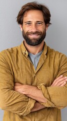 Fototapeta premium A man with a beard and a smile is wearing a yellow shirt. He is posing for a picture and has his arms crossed