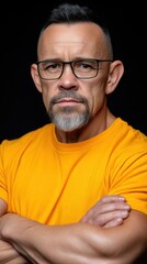 Fototapeta premium A man with a beard and glasses is wearing a yellow shirt. He is looking at the camera with a serious expression