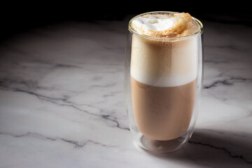 Latte in a double-walled glass cup on a marble surface, highlighting clean lines and foam texture.