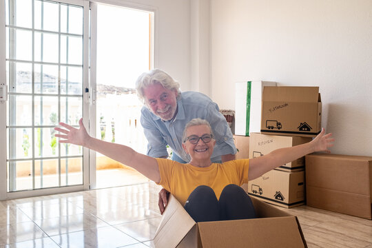 Cheerful senior couple moves into a new house, surrounded by moving boxes in an empty room, two excited seniors play with an empty box