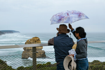 A woman holds an umbrella for her partner as he takes photos of the Twelve Apostles along the Great Ocean Road in Victoria, Australia, on a cloudy day.