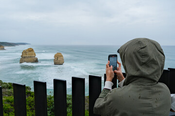 A traveler photographing the Twelve Apostles rock formations along the Great Ocean Road, Victoria, highlighting natural beauty and iconic coastal landscape
