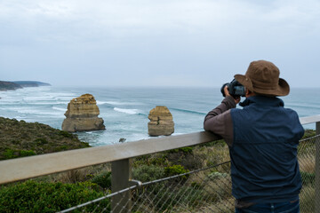 A traveler photographing the Twelve Apostles rock formations along the Great Ocean Road, Victoria, highlighting natural beauty and iconic coastal landscape