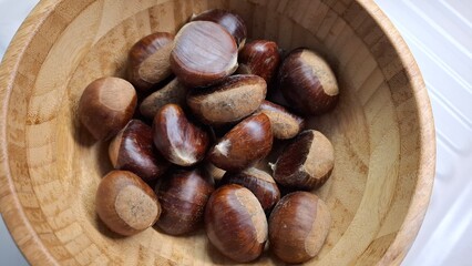 Fresh chestnuts (Castanea sativa) in a bamboo bowl — autumn close-up showing glossy texture and rustic styling, ideal for recipes, farmers markets and culinary visuals.
