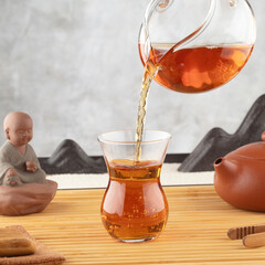 Pouring tea from teapot into glass cup on bamboo mat