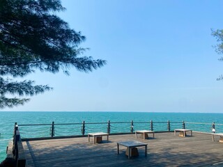 Scenic wooden deck terrace with seating area overlooking a beautiful turquoise sea and clear horizon. Tropical beach resort view, perfect for travel, vacation, and relaxation background themes.