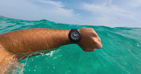 Black resin sports dive watch on a male's hand at sea. Black sports dive watch at sea. Water...