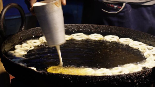 A person making jalebi by frying the batter in hot oil.