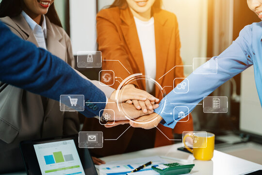 Asian business team unites hands with digital overlay icons, symbolizing teamwork, innovation, and technology for corporate success in modern office collaboration.