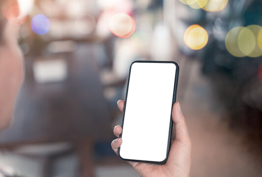 Hand holding smartphone with blank white screen in a modern cafe background, ready for mobile app mockup design and advertising online,UX design presentation, or digital marketing display