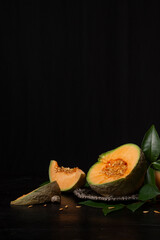 View of an open green cantaloupe melon on a tray, with a slice, black background, vertical, with copy space