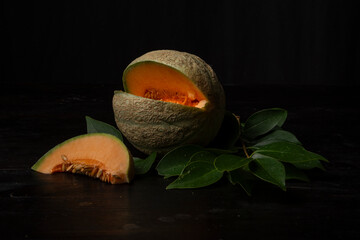 Close-up of an open green cantaloupe melon, with a slice, on a black background, horizontal, with copy space