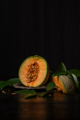 View of half a green cantaloupe melon on a tray and green leaves, black background, vertical, with copy space