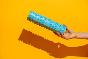 Hand holding a blue foam roller against orange background hard shadow fitness recovery at home. High quality photo