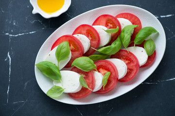 White plate with classic caprese salad on a black marble background, horizontal shot, above view