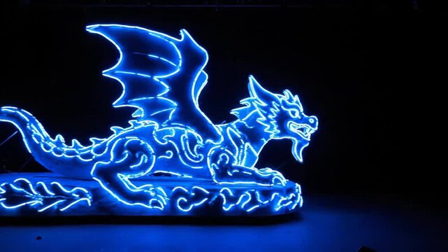 Glowing Neon Dragon Outline - A neon parade float of a dragon with a blue outline is displayed against a black background. The float features intricate designs and vibrant glowing lights.