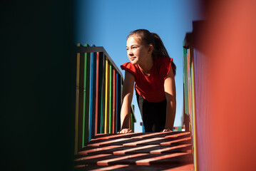 A happy child girl playing on a colorful playground structure in a sunny park, enjoying a fun and active outdoor moment.