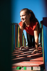 A happy child girl playing on a colorful playground structure in a sunny park, enjoying a fun and active outdoor moment.