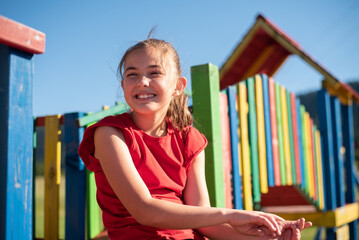 Smiling little girl playing on a colorful playground structure in a sunny park, enjoying a fun and active outdoor moment.
