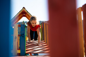 A happy child girl playing on a colorful playground structure in a sunny park, enjoying a fun and active outdoor moment.