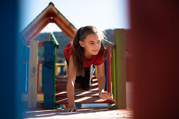 A happy child girl playing on a colorful playground structure in a sunny park, enjoying a fun and active outdoor moment.