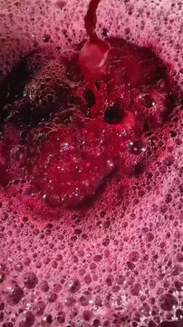 Close-up pouring dark, crimson grape must, creating a deep splash in a vessel. Vibrant, foamy layer of magenta bubbles, indicating active fermentation of winemaking process