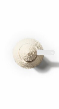Overhead view of a scoop filled with protein powder on a white surface with soft shadow casting down