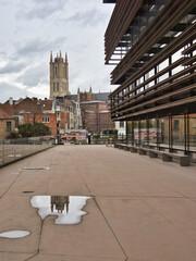 Contemporary and Old Ghent Architecture - A modern building's facade and a medieval church tower are reflected in a puddle in Ghent, Belgium.