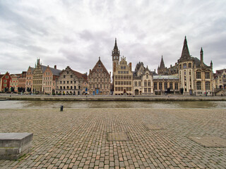 The iconic guild houses and historic buildings of Ghent stand majestically along the canal, with a wide-angle view of the cobblestone street in the foreground.