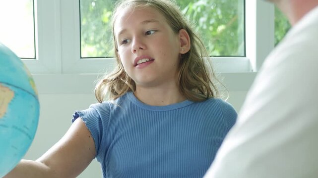 School girl is interested in the geography of different countries on a globe map model. She is interested and eager to ask her teacher questions while the teacher is teaching in the classroom.