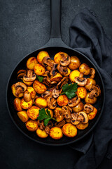 Yummy baked potatoes with mushrooms in frying pan. Black background, top view
