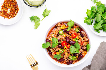Spicy beef chili con carne with red beans, sweet corn, fresh cilantro, jalapeno pepper and tomato, served on white table, top view