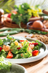 Gourmet salad with lettuce, strawberry, shrimps and walnuts on table in bright modern kitchen