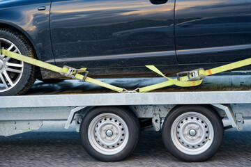 Car on tow trailer securely strapped behind a roadside truck