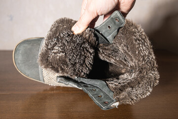 Hand holding winter boot showing thick dark gray fur interior lining. Warmth, comfort and quality...