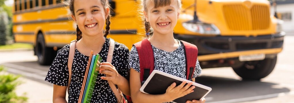 Two grade school girls getting on school bus for first day of school.
