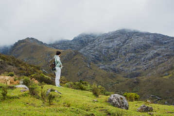 Latino man hiking in the Santurban moor in Colombia, standing with backpack and looking at misty mountains, symbolizing exploration, eco adventure, freedom, outdoor lifestyle, travel and mindfulness