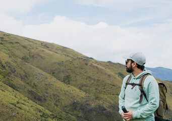 Latino man with backpack exploring Santurban moor in Colombia, standing in hoodie and cap while admiring mountain landscape, symbolizing hiking, adventure, eco tourism, outdoor lifestyle and travel