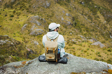 Latino man sitting on a rock with backpack in the Santurban moor, Colombia, enjoying a mindful pause surrounded by mountains, symbolizing eco travel, freedom, outdoor adventure, peace and exploration.