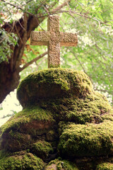 Stone Christian cross on top of rocks with moss and vegetation