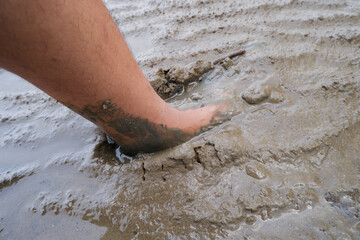 A human leg stepping into wet muddy ground, showing deep footprint in soft soil texture. Concept of nature, mud, dirt, environment, agriculture, and outdoor adventure.