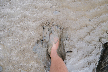 A human leg stepping into wet muddy ground, showing deep footprint in soft soil texture. Concept of nature, mud, dirt, environment, agriculture, and outdoor adventure.