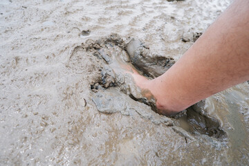 A human leg stepping into wet muddy ground, showing deep footprint in soft soil texture. Concept of nature, mud, dirt, environment, agriculture, and outdoor adventure.