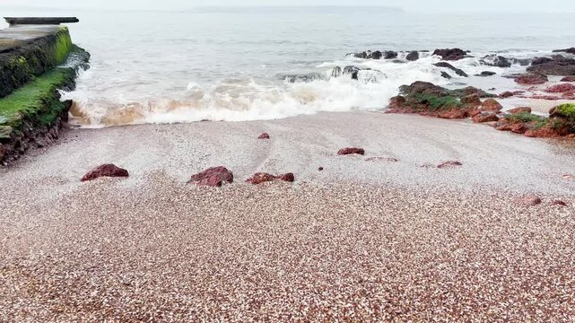 Close-up of beautiful patterns created by waves breaking and striking on red sandy coastline at a Beach in Goa, India.