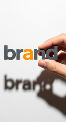 Hand holding gray and orange letters spelling "brand", against white background Shadow below creates depth, showcasing branding concept