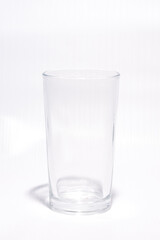 Gelas minum transparan berbahan kaca, berdiri di atas latar belakang putih. Gelas sederhana ini biasa digunakan untuk air, jus, kopi, atau minuman lainnya.
