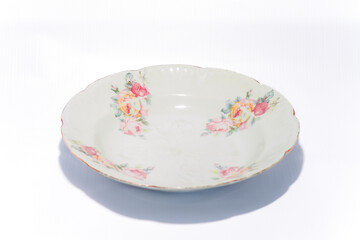 Piring keramik antik dengan motif bunga berwarna-warni, diletakkan di atas latar belakang putih. Piring tradisional bergaya vintage ini menampilkan ornamen floral yang khas, sering digunakan sebagai p
