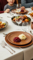 Close-up of brown plates with mashed potatoes and cranberry sauce, set on a table with blurred family background, showcasing a Thanksgiving or holiday dinner scene