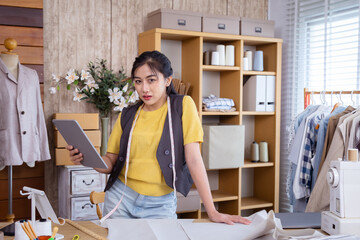 Small business fashion tailor, woman creative clothing workshop sewing boutique, Female designer uses tablet to review garment sketches, balancing digital tool with fabric planning in clothes business