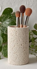A light beige, textured cylinder holds three makeup brushes with brown and peach tones.